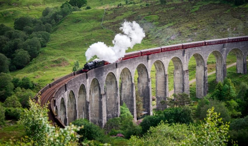 Famous Hogwarts Express steam train moving through the Scottish Highlands on Glenfinnan Viaduct