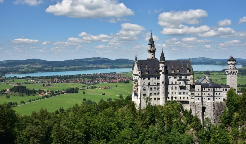 Neuschwanstein Castle on a hilltop overlooking the Bavarian Alps and Forggensee lake under a blue sky