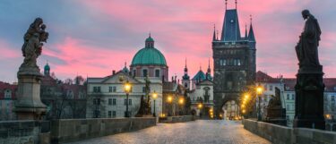 Charles Bridge at twilight with lit street lamps, statues, and the Old Town Bridge Tower