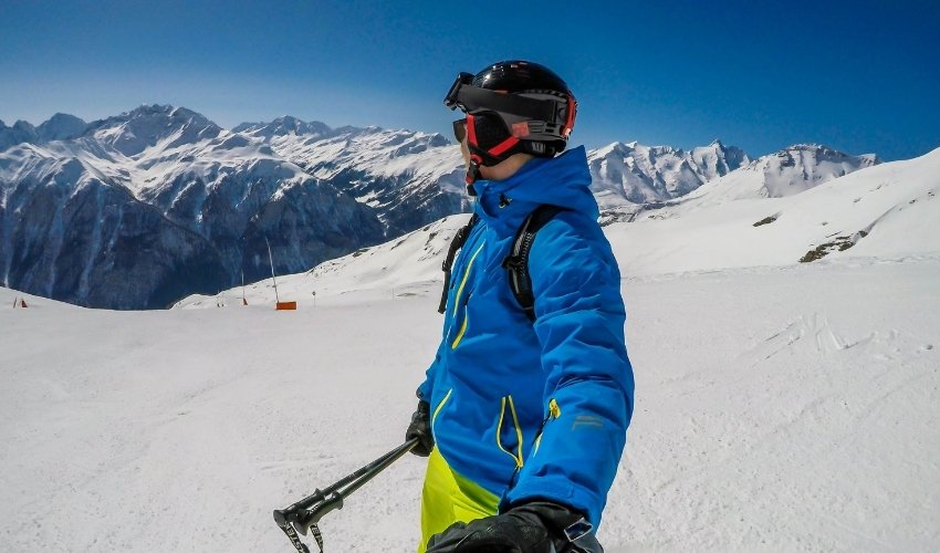 A skier in a blue jacket and lime green pants standing on a snowy mountain ridge in the Dolomites