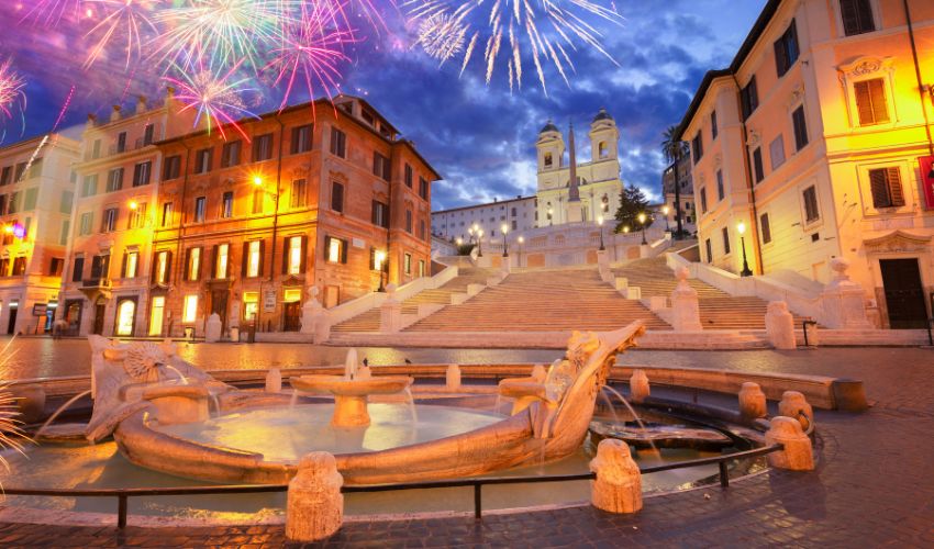 Colorful fireworks bursting over a historic city square with a grand stone staircase and a fountain