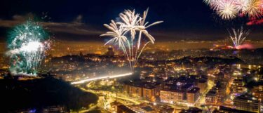 Aerial view of a city at night with vibrant fireworks exploding over illuminated buildings and streets