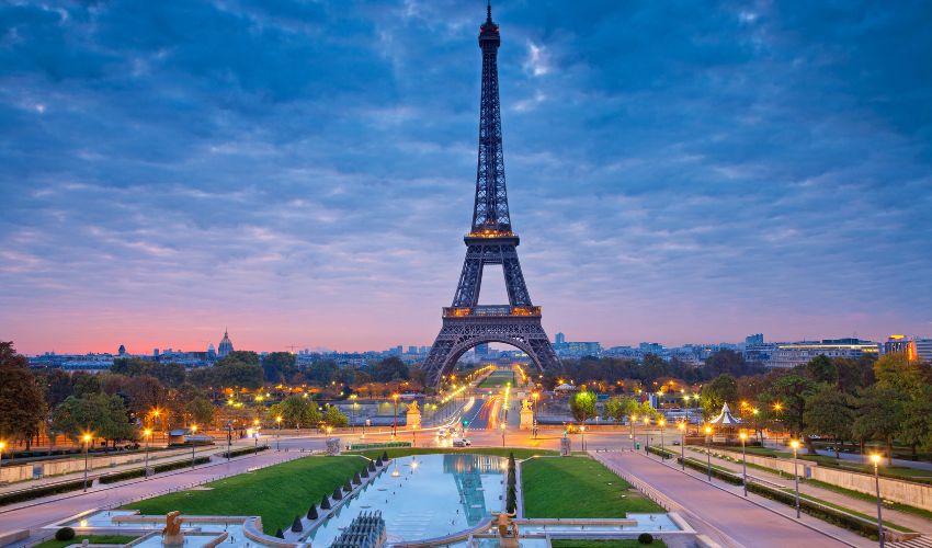 The Eiffel Tower at dawn with a clear sky and garden paths in the foreground
