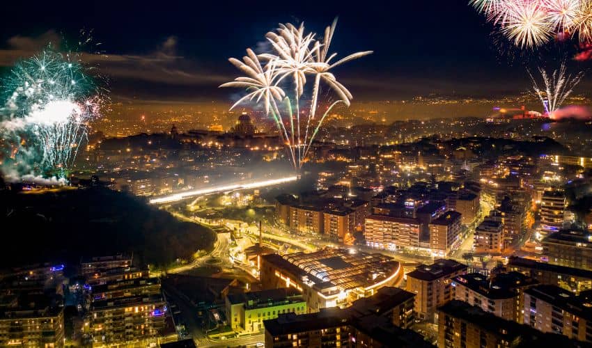 Aerial view of a city skyline illuminated by colorful New Year's Eve fireworks at night